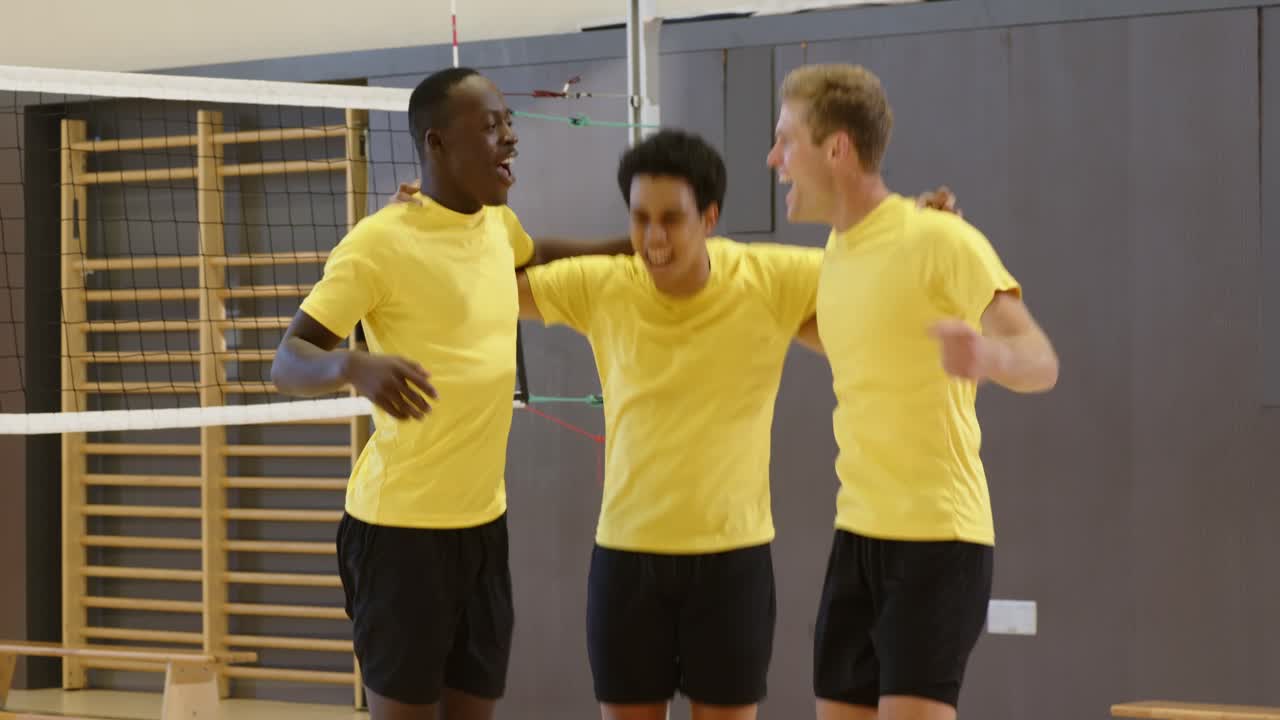 Trio maschile eterogeneo in maglia gialla che festeggia un punto dopo un servizio blu sul campo da palestra vicino alla rete.