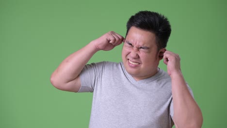 young handsome overweight asian man against green background