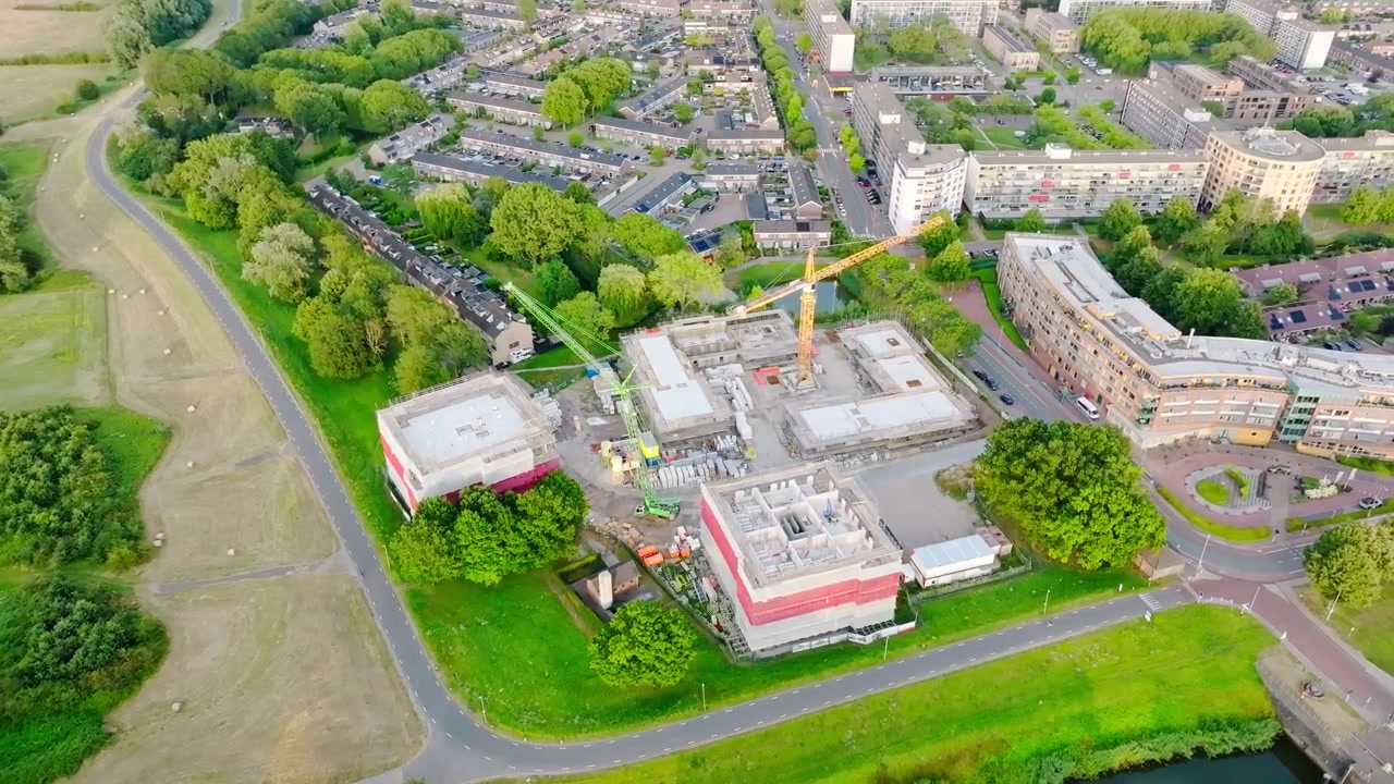 Veduta aerea con drone di un grande cantiere residenziale con gru a torre che costruiscono nuovi condomini in un verde quartiere residenziale olandese in una soleggiata giornata estiva