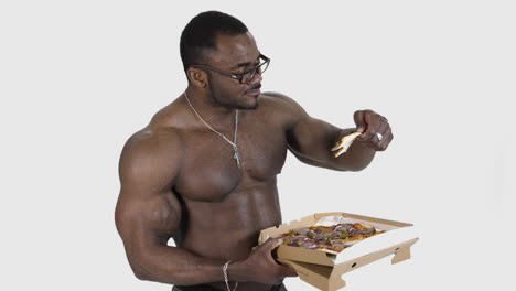 african american man eating pizza. black muscular man enjoying delicious pizza from carton package. sportsman eats unhealthy food isolated in studio. slow motion.