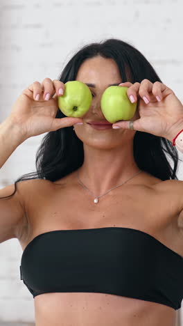 pretty brunette caucasian woman standing near table with healthy apples and playing with it. healthy diet food concept vertical video
