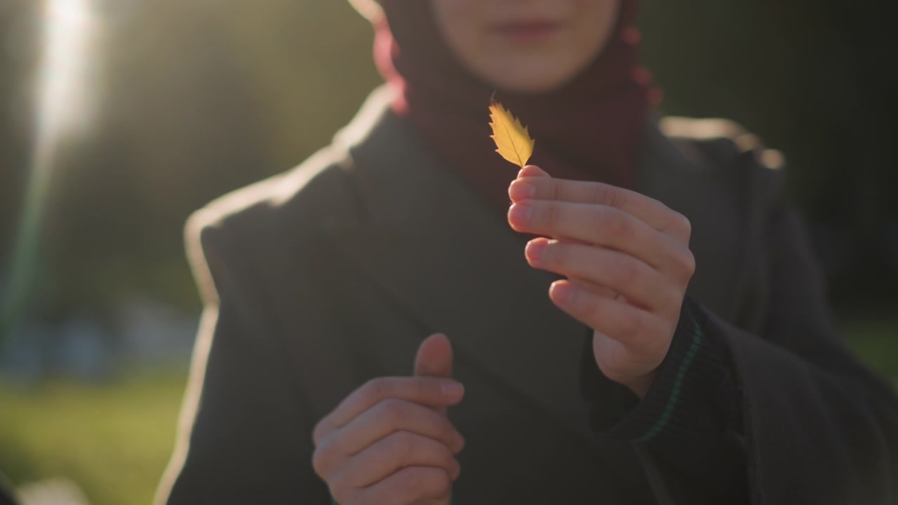 Giovane donna che tiene una piccola foglia autunnale gialla all'aperto.