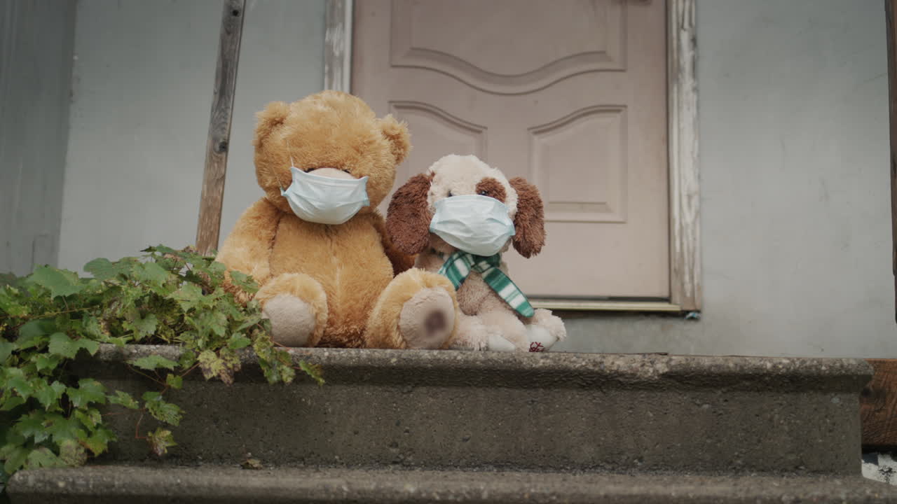 보호 마스크를 입은 두 명의 장난감이 집 문 ⁇ 에 앉아 있습니다. 자립과 희망 개념의 끝