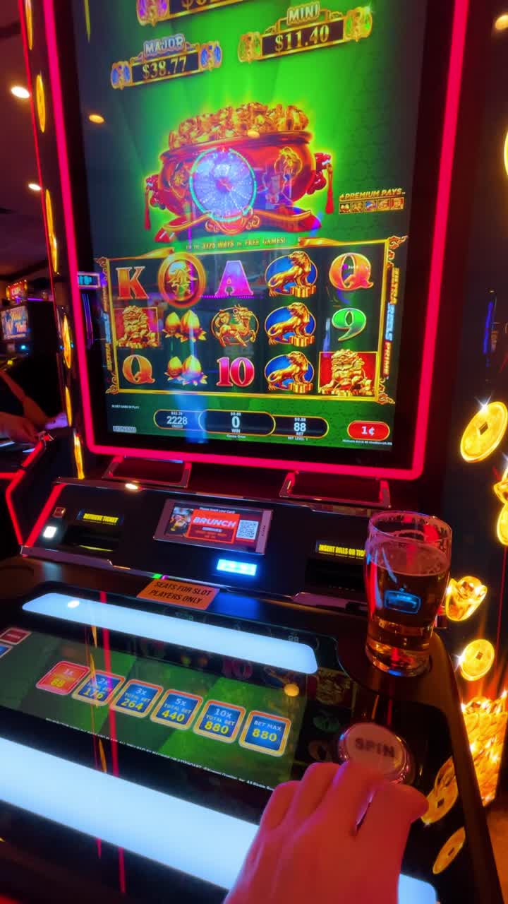 New York, USA, 11 maggio 2025: Persona che gioca a una slot machine con un bicchiere di birra al casinò. Scatto in soggettiva di una mano su un pulsante di una slot machine accanto a un bicchiere di birra in un casinò.