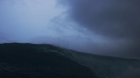 Ocean-wave-crashes-spraying-droplets-into-barrel,-low-angle-view