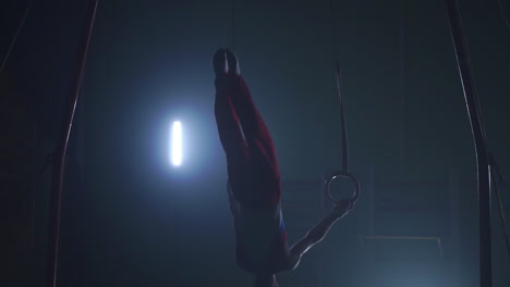 gymnast on a dark background stands on his hands using rings in the air. performs rotation in the olympic program