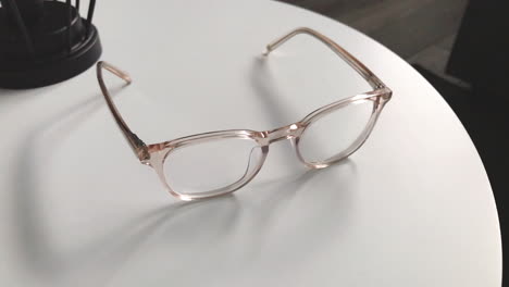 modern eyeglasses in light colour lie on a white table, bright glasses frame, slow motion footage