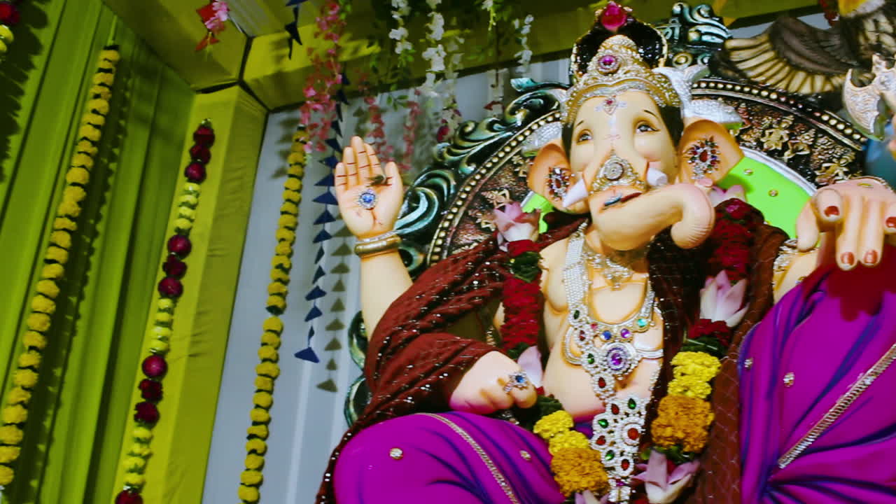 Close angle of Ganpati idol decorated with jewellery, flowers and crown inside pandal. Ideal for Ganesh Chaturthi, devotion, prayer, worship, Indian culture and spiritual festival HD 4K clips