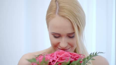 Lächelnde-Blonde-Frau-Riecht-Rosa-Rosen