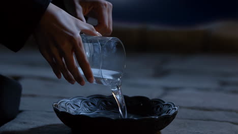 person pouring water from a glass into a decorative bowl
