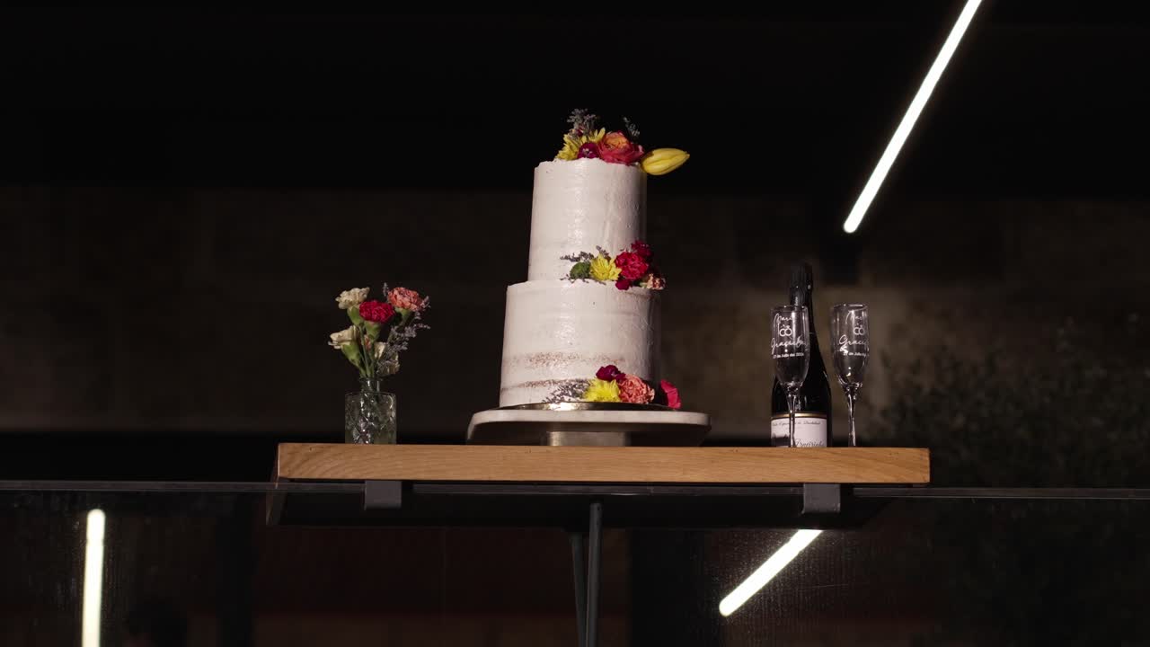 wedding cake adorned with flowers, surrounded by glasses and champagne bottle on wooden stand