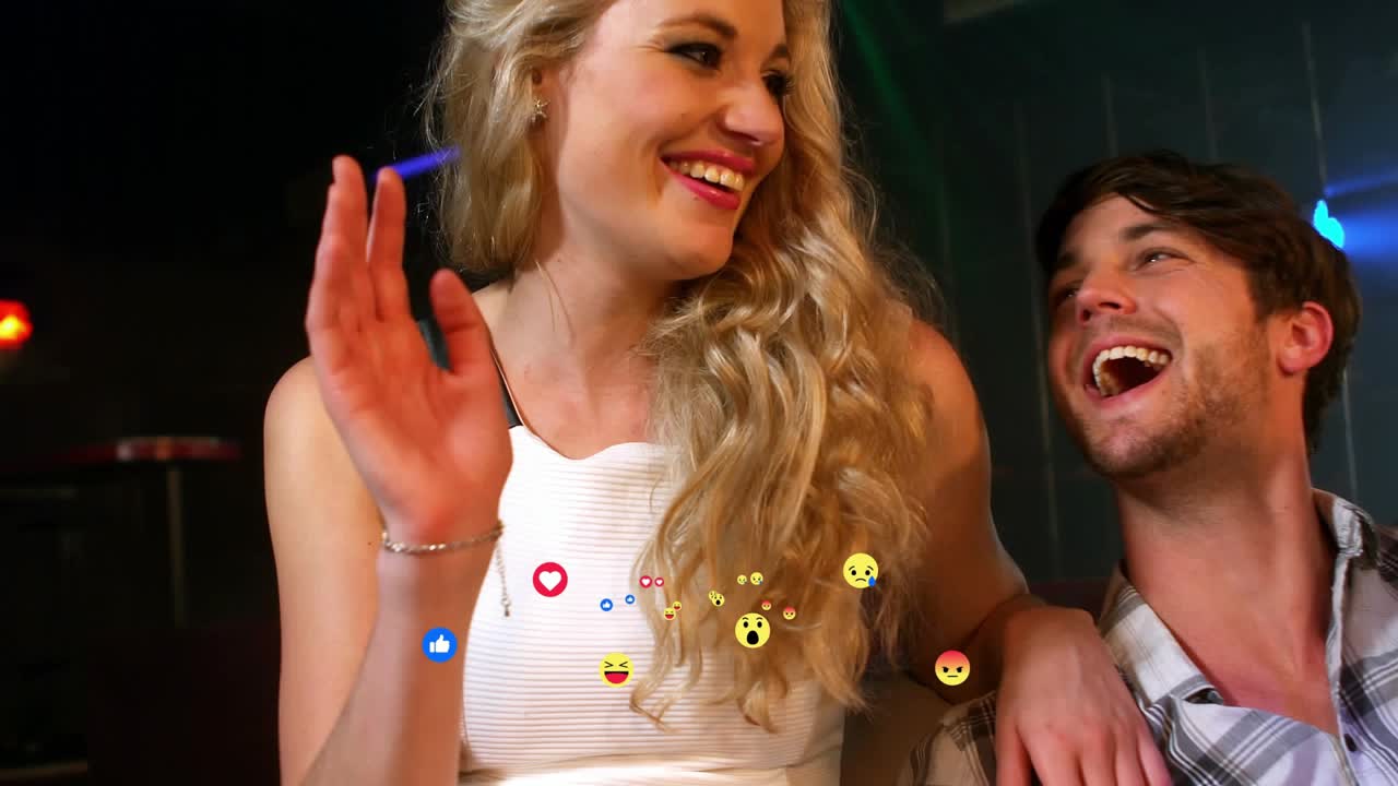 Three friends laughing in club, blonde raising hand, social media reactions appearing lower center