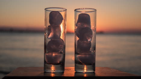 vasos con hielo derretido contra el fondo del mar y el atardecer