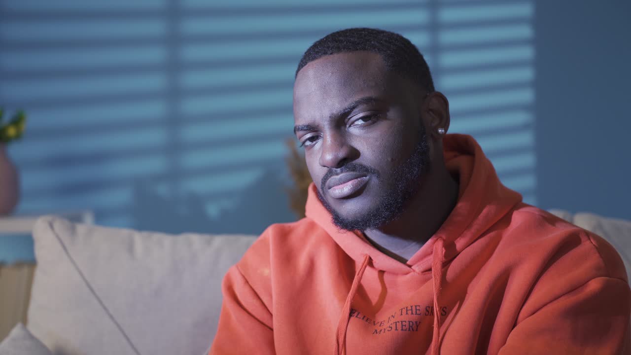 Unhappy black man at home alone looking at camera