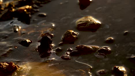 calm waves kissing a frozen rocky lake shore in poland during sunset - close up