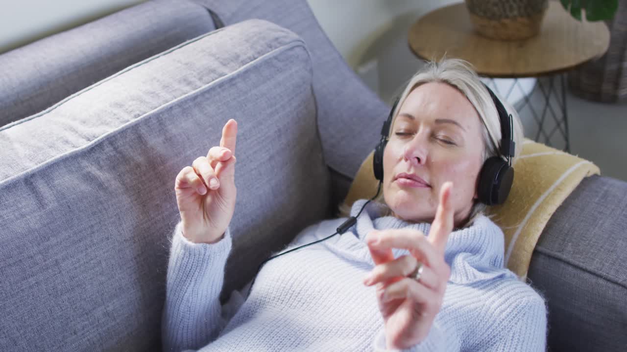 거실에서 소파에 누워 헤드폰을 착용 한 편안한 고위 백인 여성