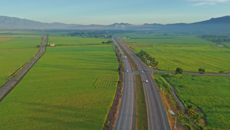 traffic over duarte highway crossing countryside rice fields at bonao in dominican republic. aerial drone shot
