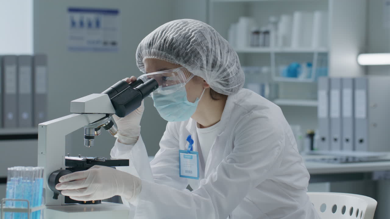 вЂ‹вЂ‹Scientist in Protective Uniform Using Microscope and Taking Notes in Laboratory