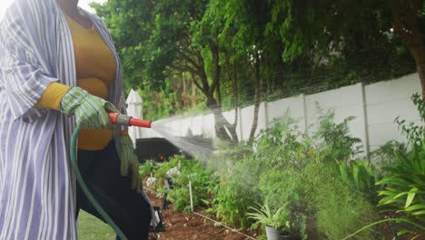 video de la sección media de tamaño plus mujer afroamericana regando flores en el jardín