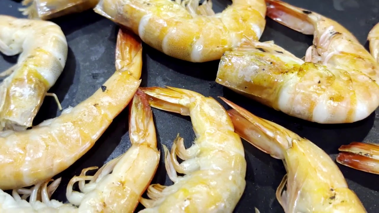 Primo piano di gamberi freschi che sfrigolano su una padella calda da barbecue, catturando frutti di mare succosi, vapore che sale e deliziosi sapori grigliati in una scena di cucina.