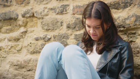 unhappy young woman with mental health issues leaning against wall