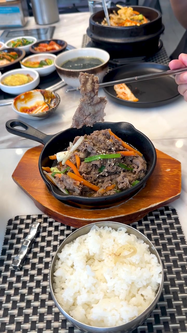 Bidikan close-up tangan menggunakan sumpit untuk mengambil daging sapi dari wajan panas yang mendesis.
