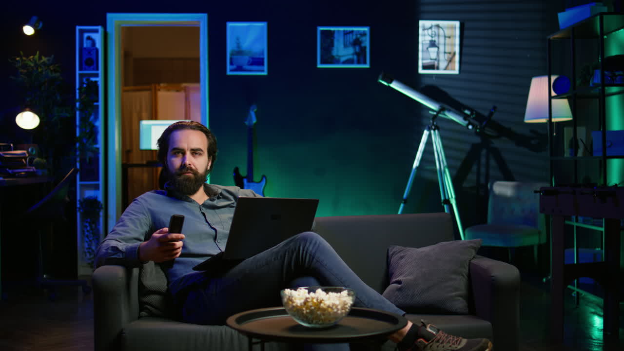 teletrabajador escribiendo correos electrónicos en la computadora portátil en casa mientras ve la televisión