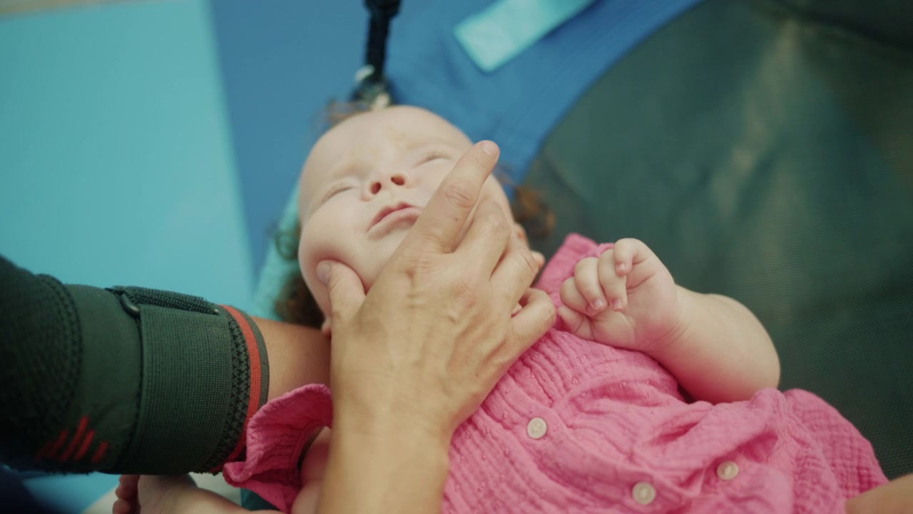 Terapista che esegue esercizi fisici sul viso di un neonato, assistendo con la salute dello sviluppo e le cure mediche durante la riabilitazione.