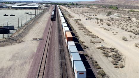 aerial drone following moving freight trains in barstow desert in the usa