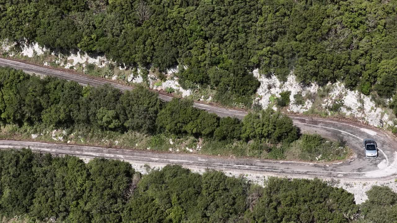 Luftfoto af sølvfarvet cabriolet, der kører på snoet bjergvej i Sokraki, Korfu, Grækenland