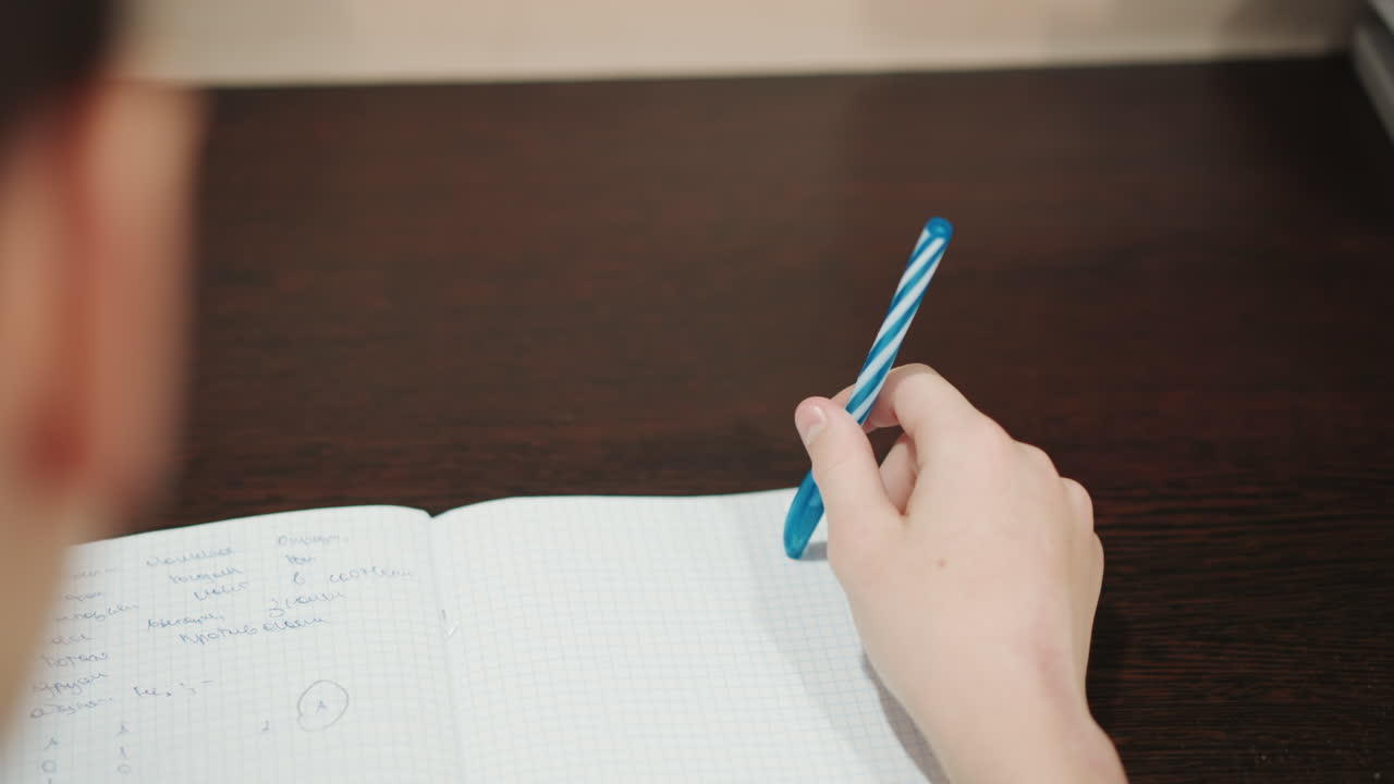 El niño se concentra en su tarea de escritura. Un niño pequeño practica intensamente con un bolígrafo de tinta azul, en una escena de aprendizaje infantil que lo muestra completamente enfocado en escribir en un escritorio de madera.