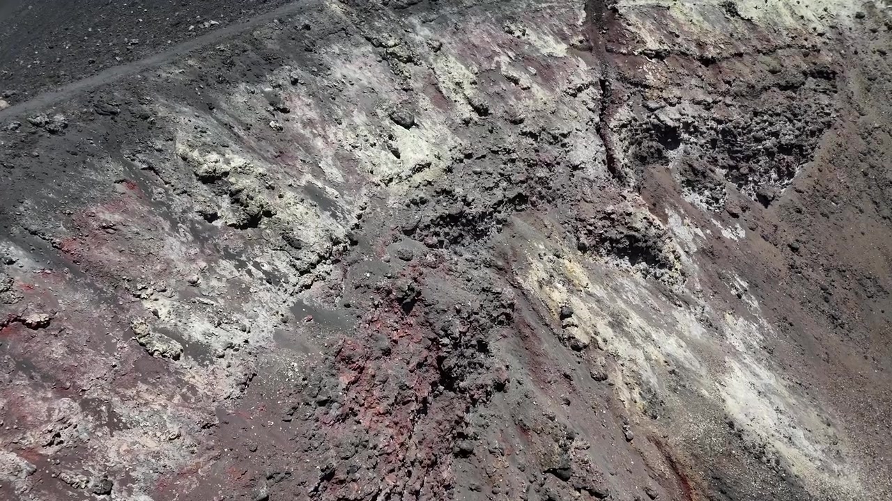 Aerial close-up of the intricate volcanic textures and colorful mineral deposits inside the Pico do Fogo crater, Cabo Verde, showcasing unique geological formations and basaltic rock