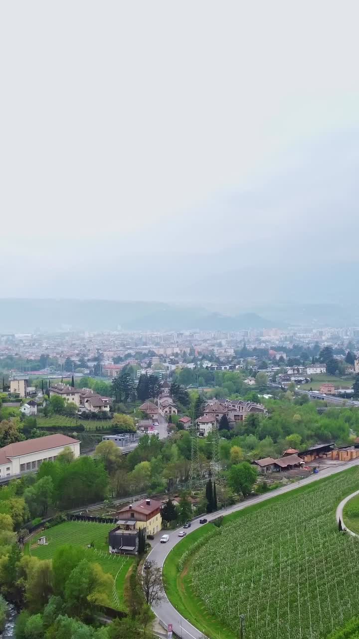 A vertical drone shot near Roncolo Castle reveals village traffic and green vineyards below.