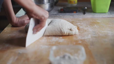 la masa recién amassada se corta con una herramienta de raspado en la mesa de la cocina de madera, filmada en primer plano en cámara lenta de mano