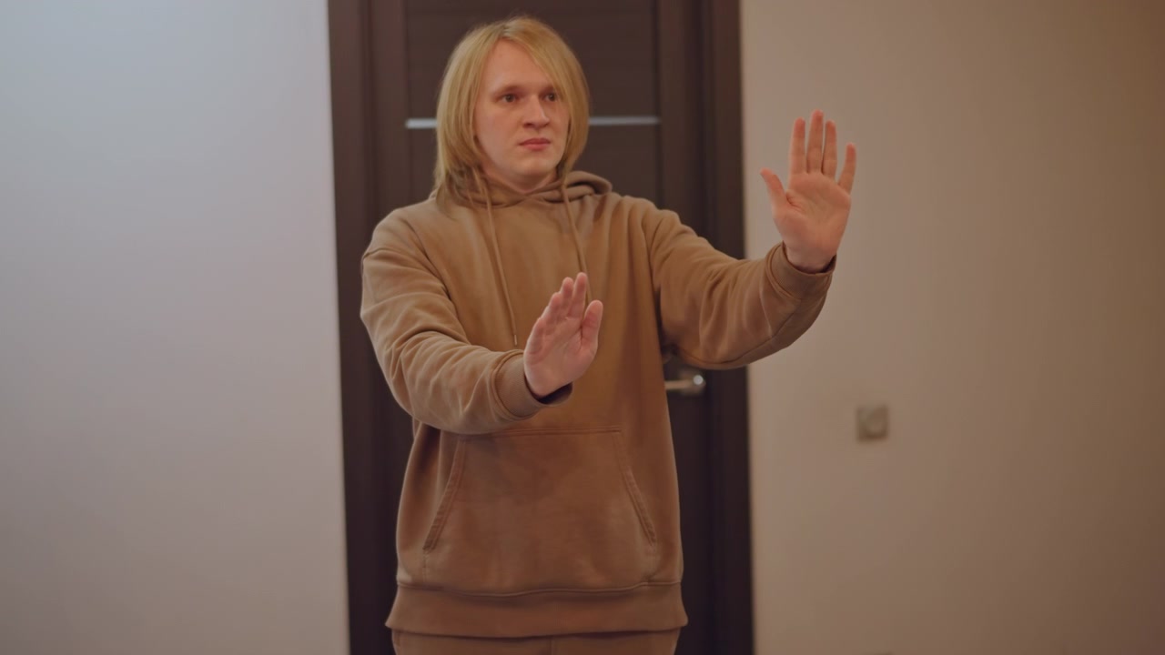 White musician conducting at home hallway, expressive hand gestures, hoodie, focused rehearsal, door background, teaching posture, practicing rhythm for virtual lesson, mentor energy