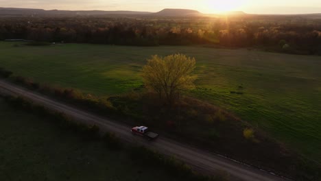 drone shot of a side view of a truck driving on a dirt road in the sunset, moving over to follow behind the truck, then overtaking the truck