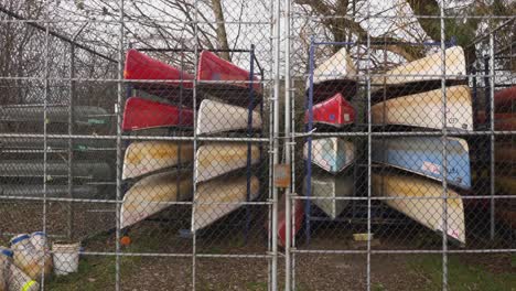 colorful canoes stored stacked organized behind a locked fence during autumn fall off season at a city owned public park