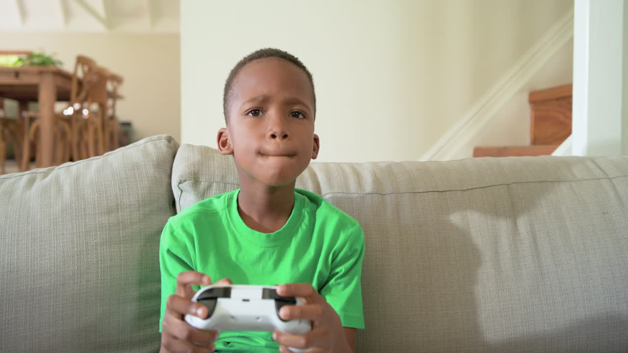 African American child sitting legs crossed on couch holding white gamepad reacting to game start