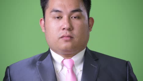 young handsome overweight asian businessman against green background