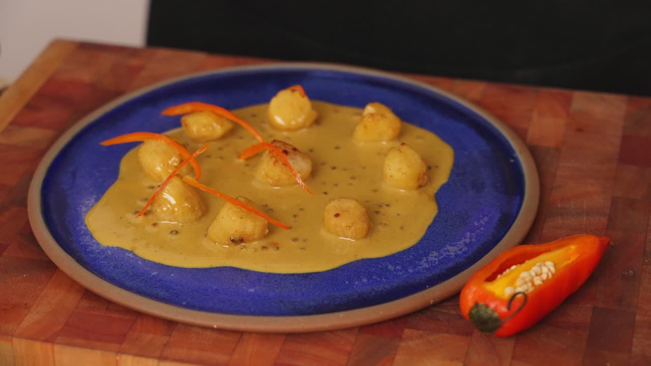 talentoso chef adornando el picante plato de vieiras de marisco con curry amarillo con pinzas, pimiento rojo en juliana encima de cada vieira, tiro de cerca