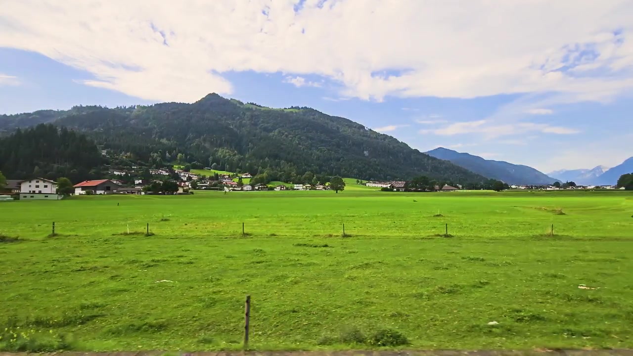 ヨーロッパの穏やかな夏の谷間の旅の風景。オーストリアを通過する列車の車窓から、畑、木々、納屋、山林が流れていく。