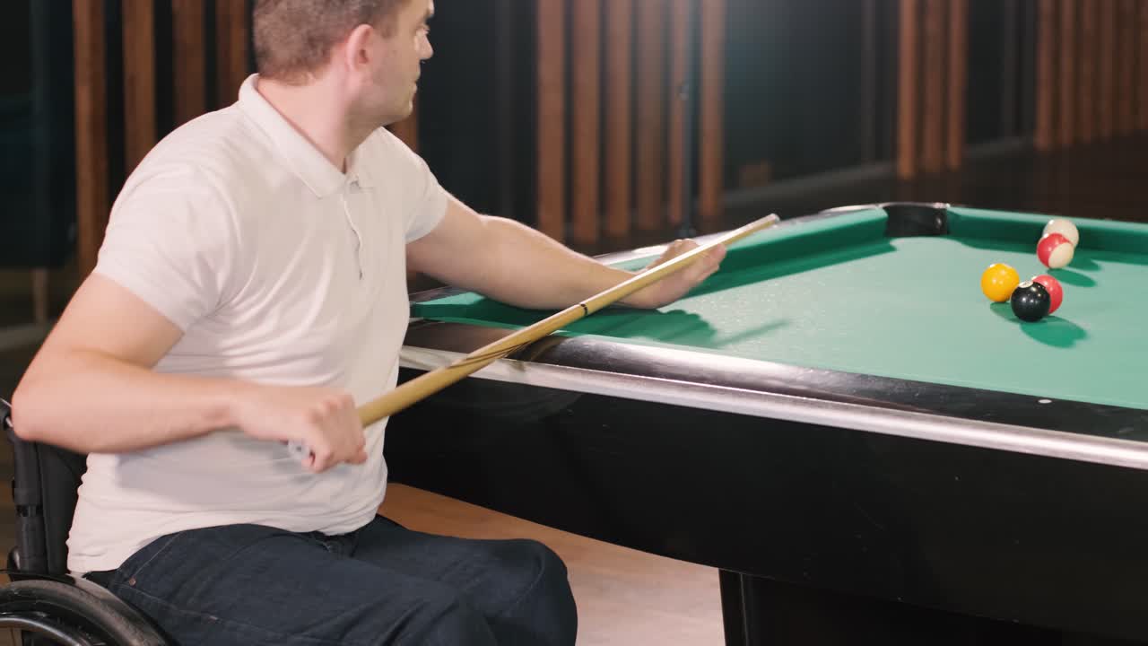 Adult men with disabilities in a wheelchair play billiards in the club