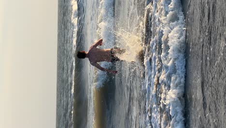 Toma-Vertical-De-Un-Joven-Corriendo-Hacia-El-Mar-Y-Saltando-Al-Agua-Durante-Las-Vacaciones-De-Verano.