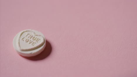 hand picking up heart candy with romantic message true love on pink background