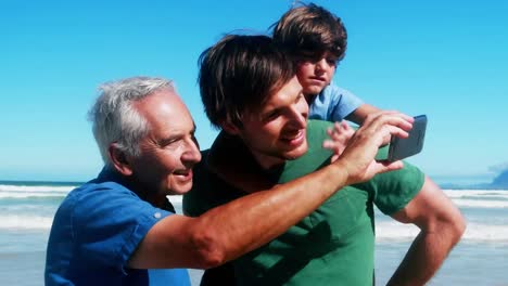 formas abstractas sobre vibraciones texto contra abuelo, padre e hijo teniendo una videollamada en la playa