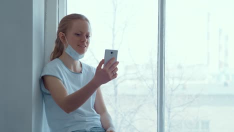 woman in hospital gown using smartphone by window