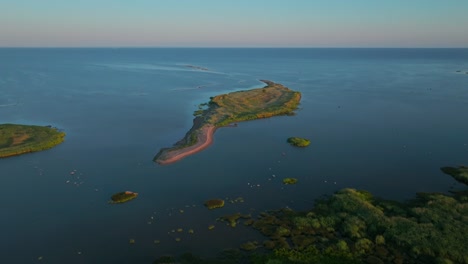 Drone shot of green island islet in summer, moving left to right revealing green coastline