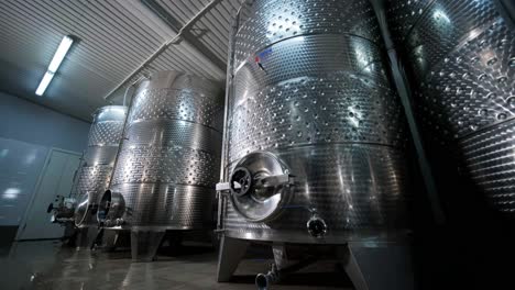 a happy successful farmer or winemaker is walking in the middle of wine tanks and checking a fermentation grade of high quality wine production in a modern winemaking facility or winery.