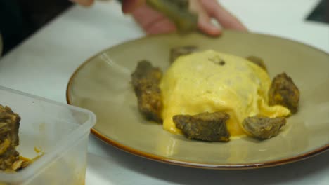 pieces of meat being placed onto plate with freshly fried egg filmed as close up shot