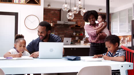 father helps children with homework whilst mother holds baby
